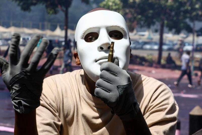 a masked demonstrator holds an empty ammunition shell used by police