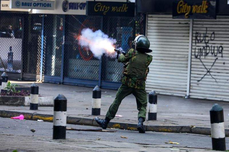a police officer fires tear gas at demonstrators