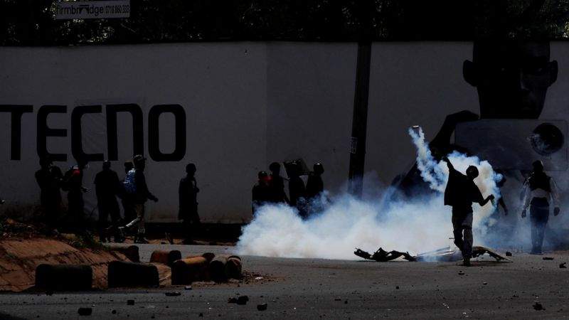 a protester throws a tear gas canister back at police