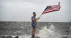 Youtuber Mark Peyton Holds A US Flag As He Poses For His Brother Matt Peyton On The Shoreline Ahead 300x162