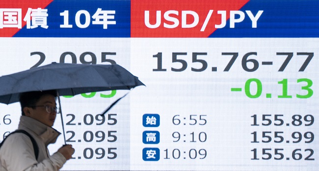 A pedestrian walks past an electronic quotation board displaying the foreign exchange rate of the Japanese yen against the US dollar (R) along a street in Tokyo on February 25, 2026. (Photo by Kazuhiro NOGI / AFP)