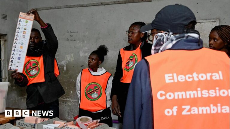 An election official displays a ballot paper as observers look on during the counting of votes after the polls closed at a polling station in Lusaka, Zambia