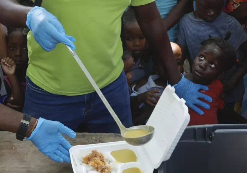 a server ladles soup into a container as children line up to receive food at a shelter for families displaced by gang violence in port au prince haiti march 14 2024 a server ladles soup into a container as children line up to receive food at a shelter for families displaced by gang violence in port au prince haiti march 14 2024