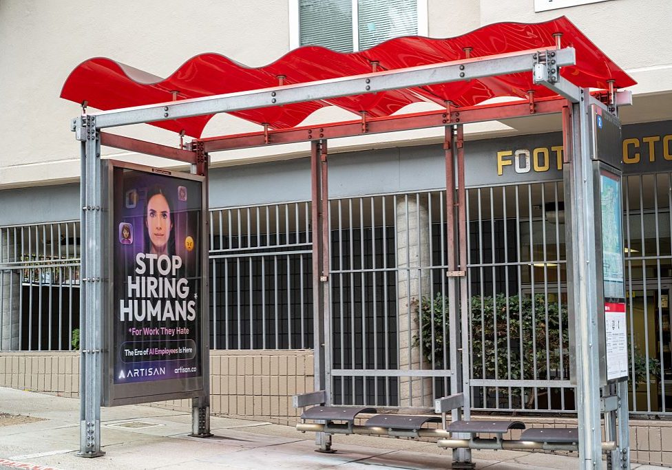 Bus stop shelter with red canopy and ad for Artisan AI reading "Stop Hiring Humans" and "For Work They Hate" on city sidewalk, San Francisco, California, September 30, 2025. (Photo by Smith Collection/Gado/Getty Images)